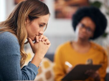 Client reflecting during holistic psychotherapy session with therapist taking notes