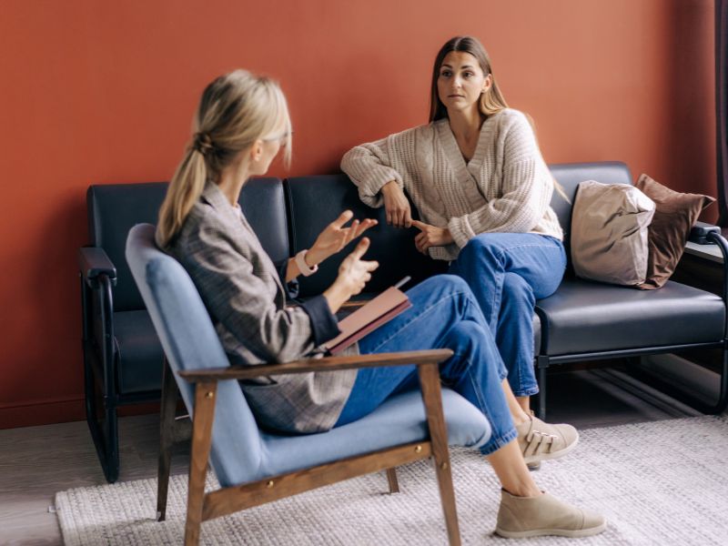 A woman and a psychotherapist conduct a holistic psychotherapy session in a therapy office.