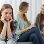 A girl sits alone off to the side of a group of others, demonstrating social anxiety.