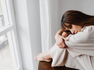 A woman sits near a window, experiencing emotional numbness