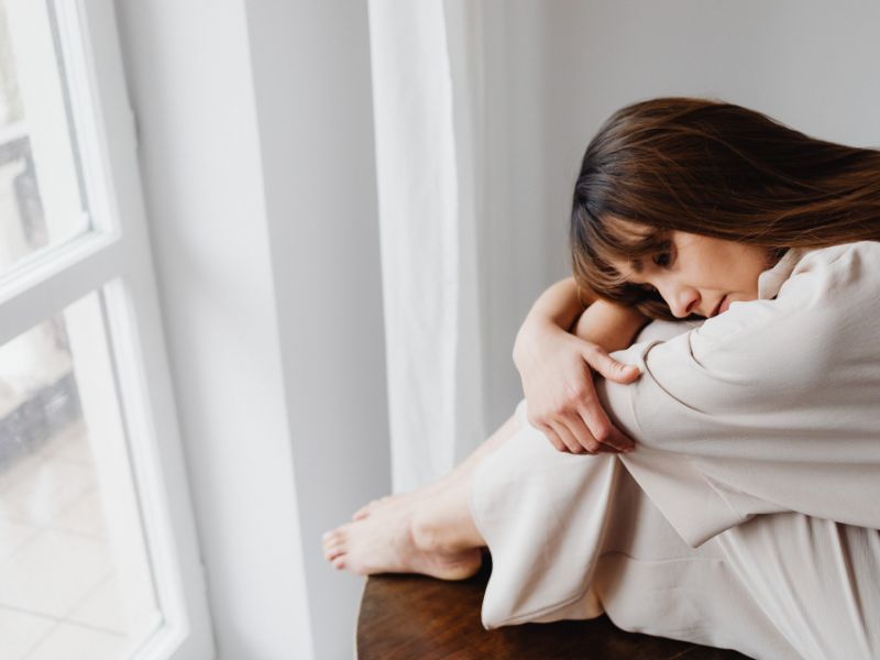 A woman sits near a window, experiencing emotional numbness